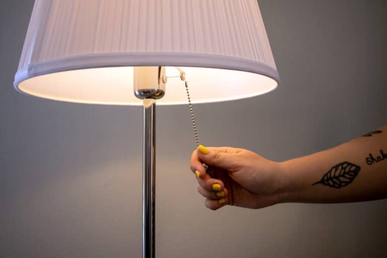 Kuvan ulkopuolelta kurottuva käsi on sammuttamassa päällä olevaa jalkalamppua.