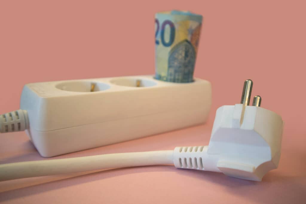 Valkoinen jatkojohto, jonka yhteen pistokkeeseen on kääritty 20 euron seteli.