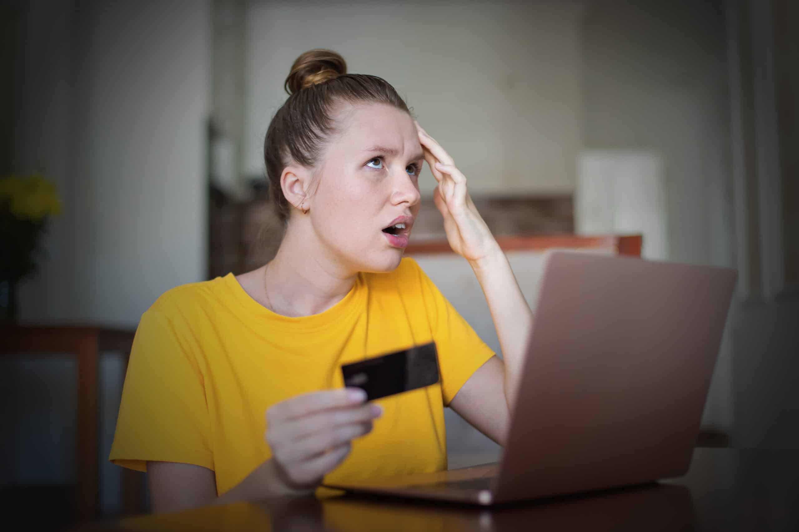 Nuori henkilö raapii hermostuneena otsaansa ja pitelee toisessa kädessään luottokorttia. Hän istuu tietokoneensa äärellä.
